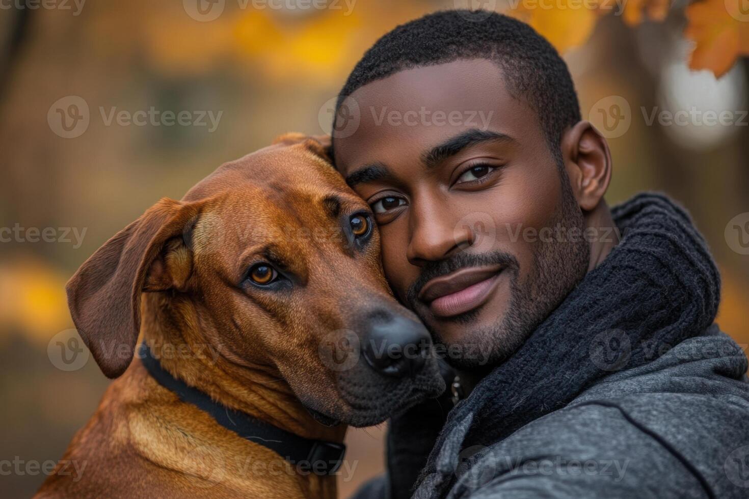 Close up of a smiling person hugging a brown dog with leaves out of focus in the background during fall season photo