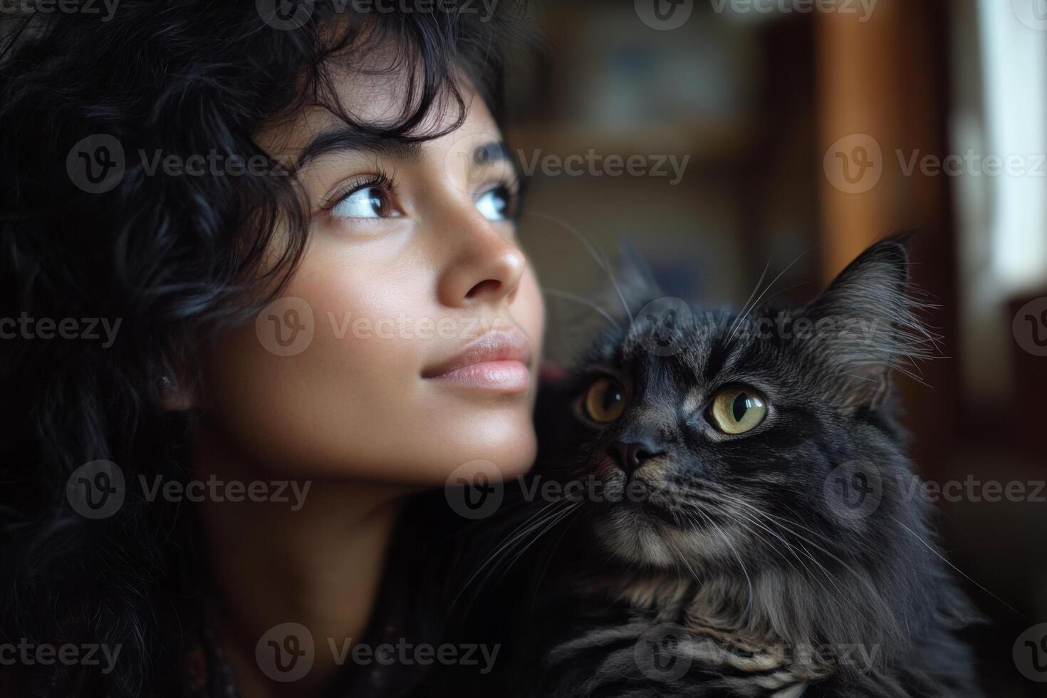 Woman looking upward next to a black cat. Furry feline looking away with light shining from window. Soft indoor light and peaceful friendship. photo