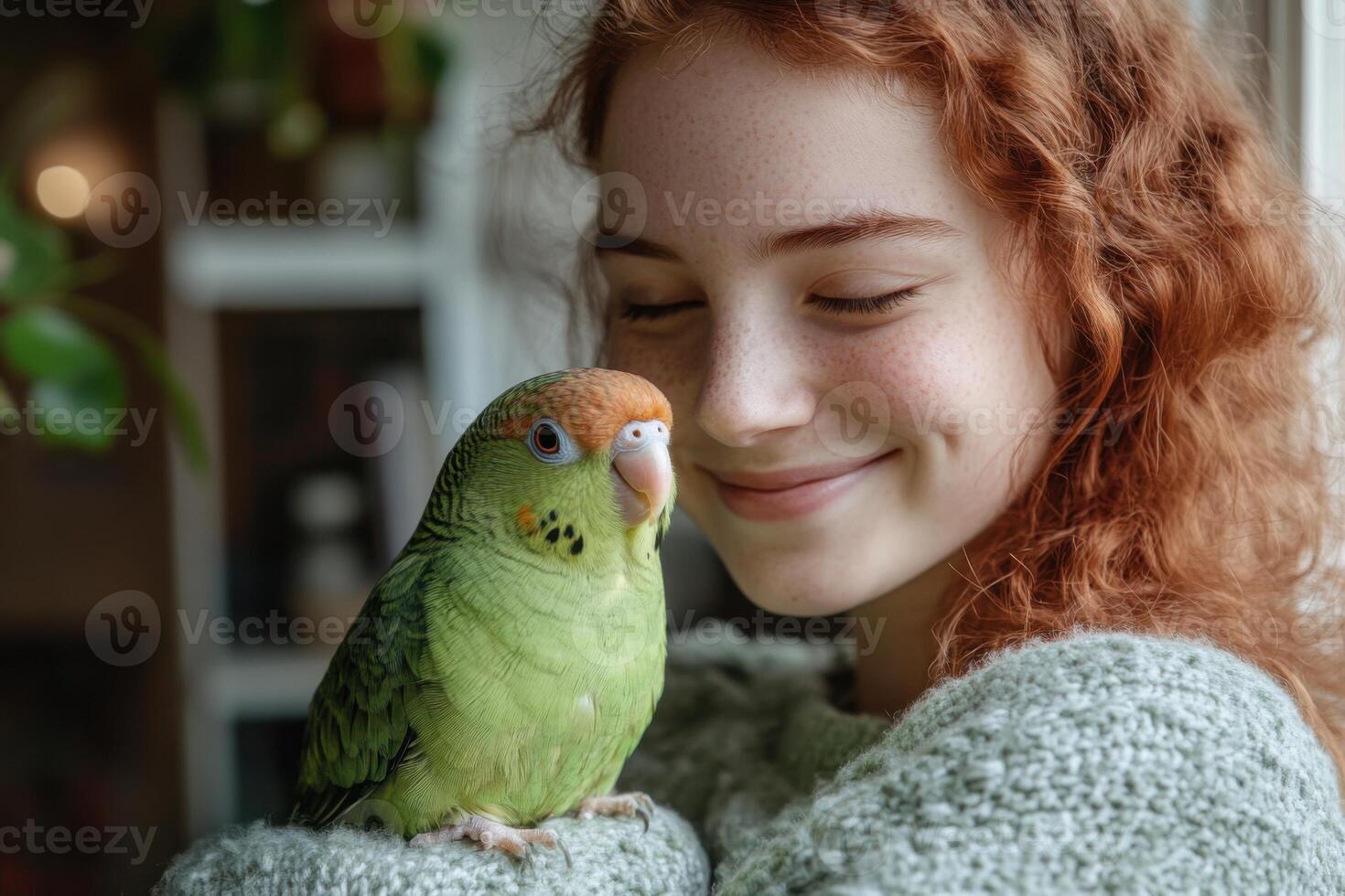 Smiling woman with red curly hair holds a green parrot gently. Bird sits comfortably. Bright indoor scene near a window with plants. photo
