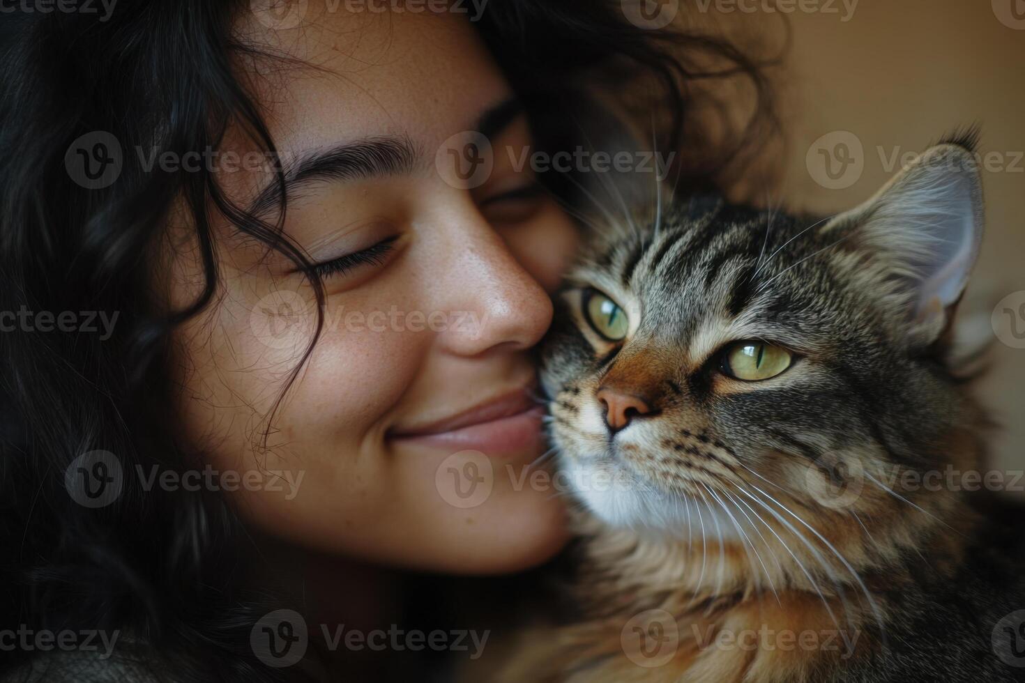 Young woman embraces tabby cat indoors. Smiling girl with curly hair snuggles with feline friend. Close up portrait of affection and love. photo
