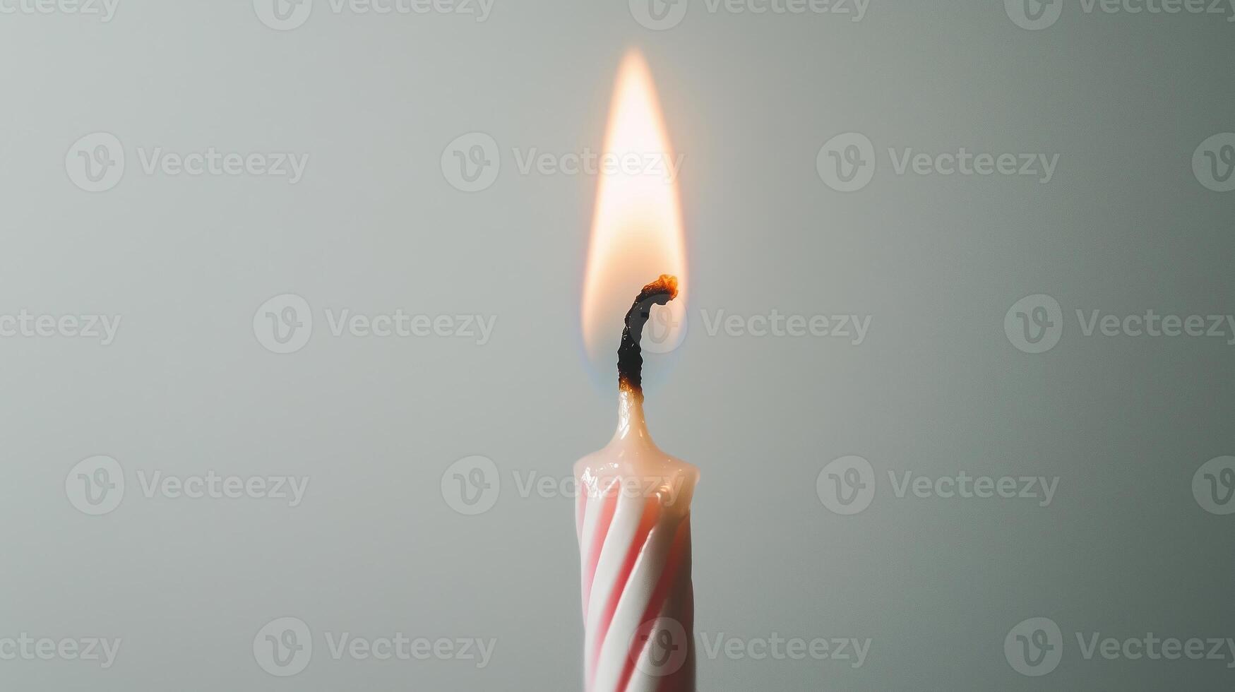 A single lit candle with a red and white striped candle photo