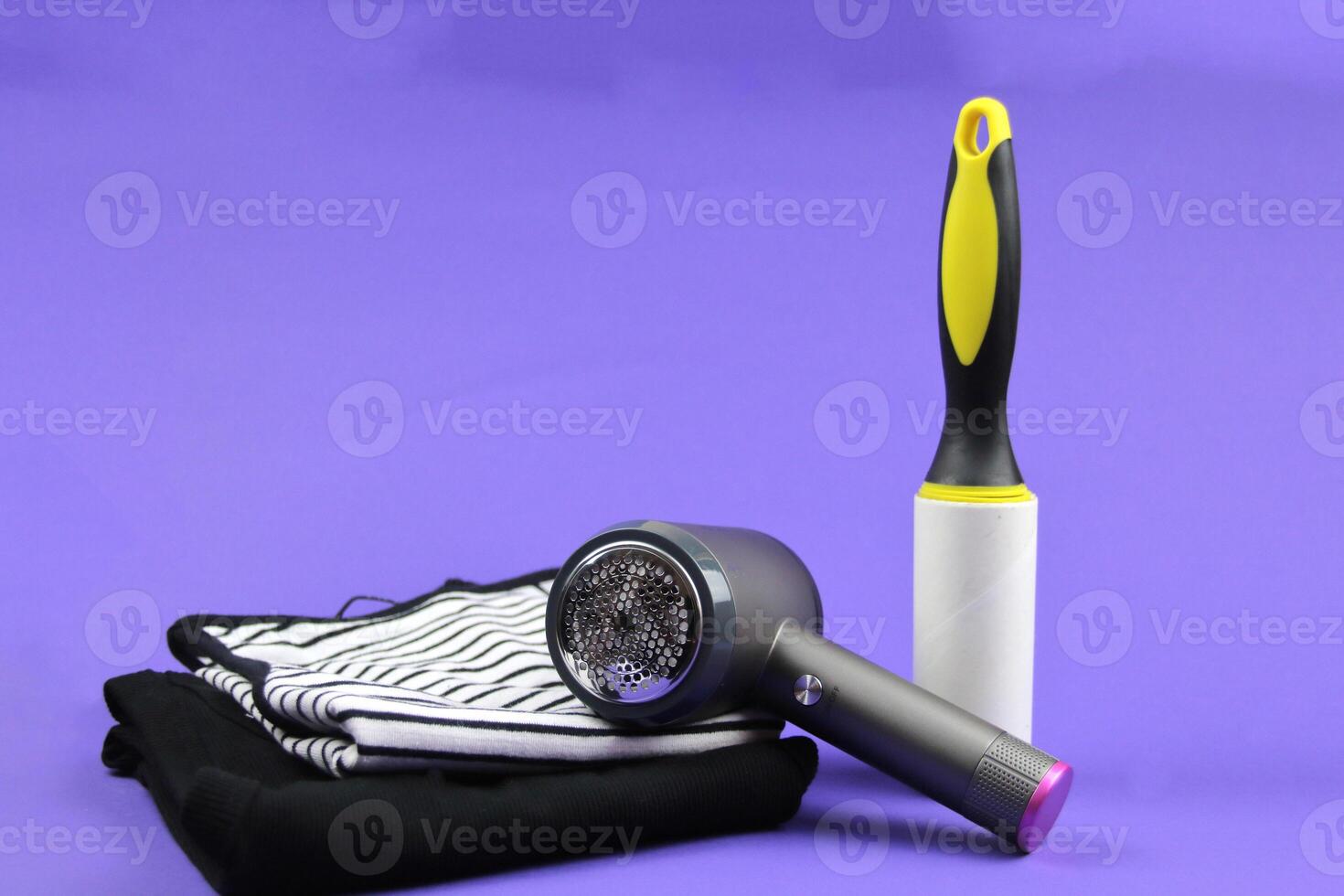 Two T-shirts are lying on a purple background, next to them is a lint machine and a clothes roller. Concept of caring about cleaning clothes. photo