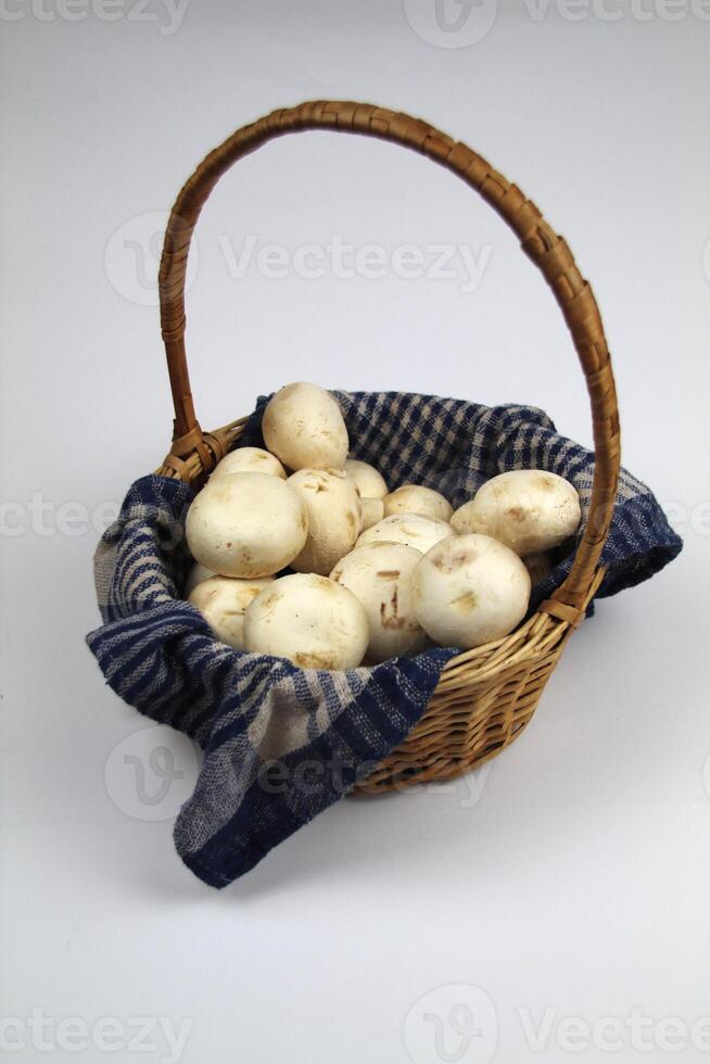 Champignons in a wicker basket, lying on a woven towel on a white background photo