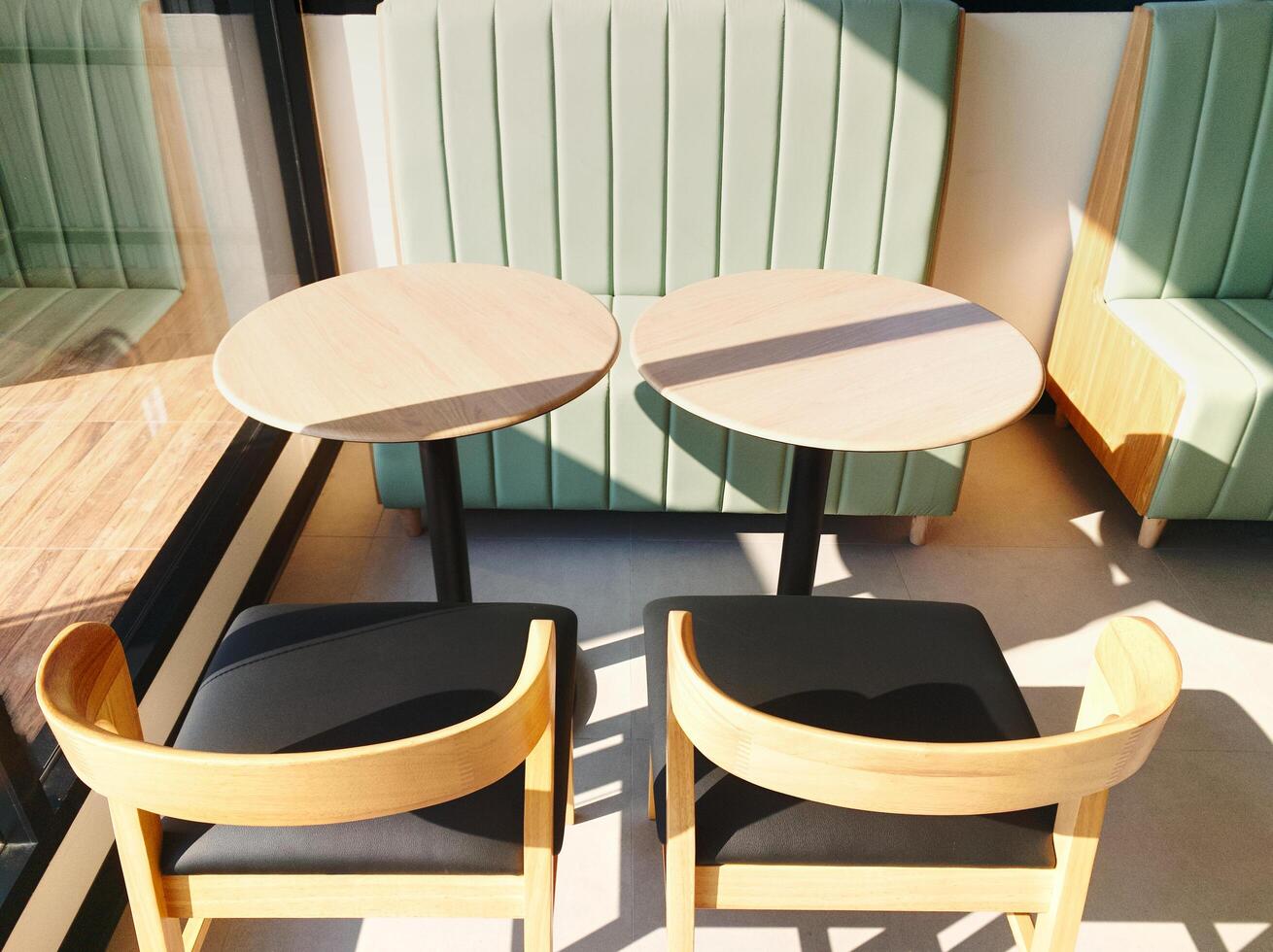 black leather cushioned wooden table and chairs in coffee shop placed next to glass door receives morning sunlight. photo