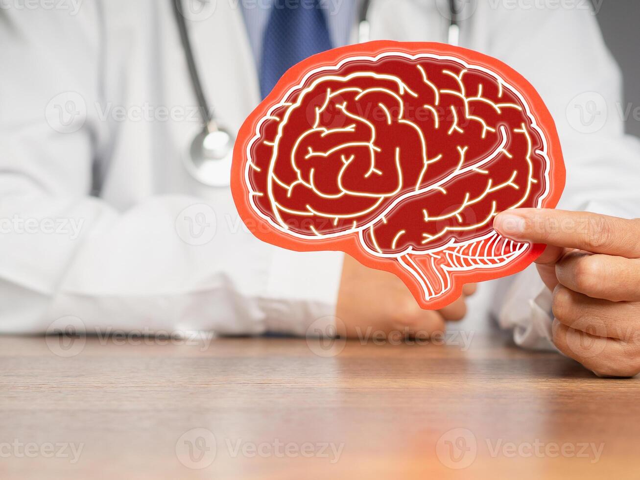 Close-up of a doctor in a uniform holding a brain symbol made from red paper while sitting at the table. photo