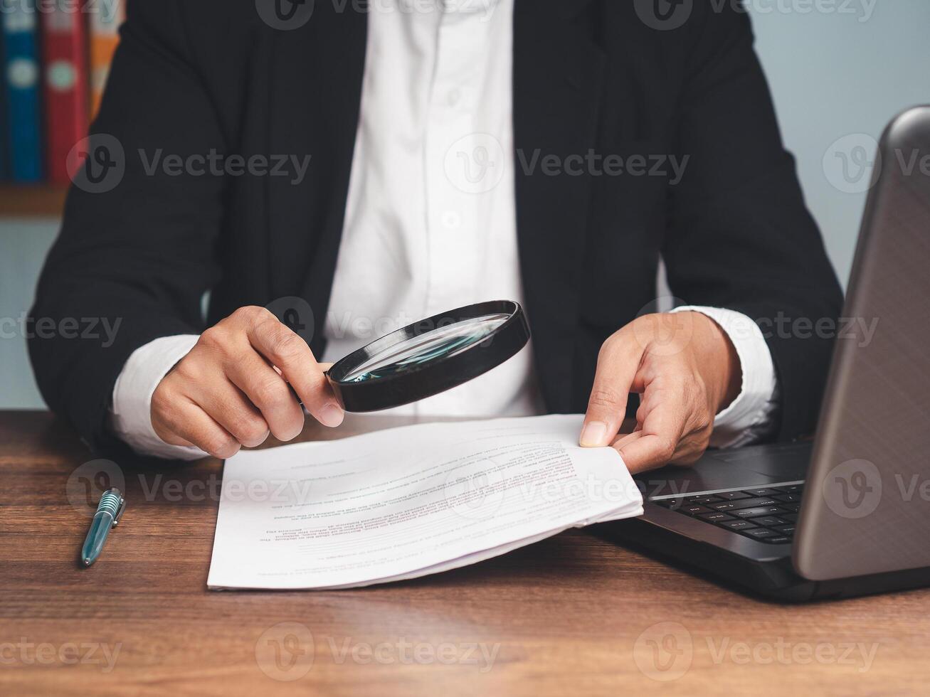 Close-up of a businessman's hand holding a magnifying glass and looking at reading documents while sitting at the tabl photo