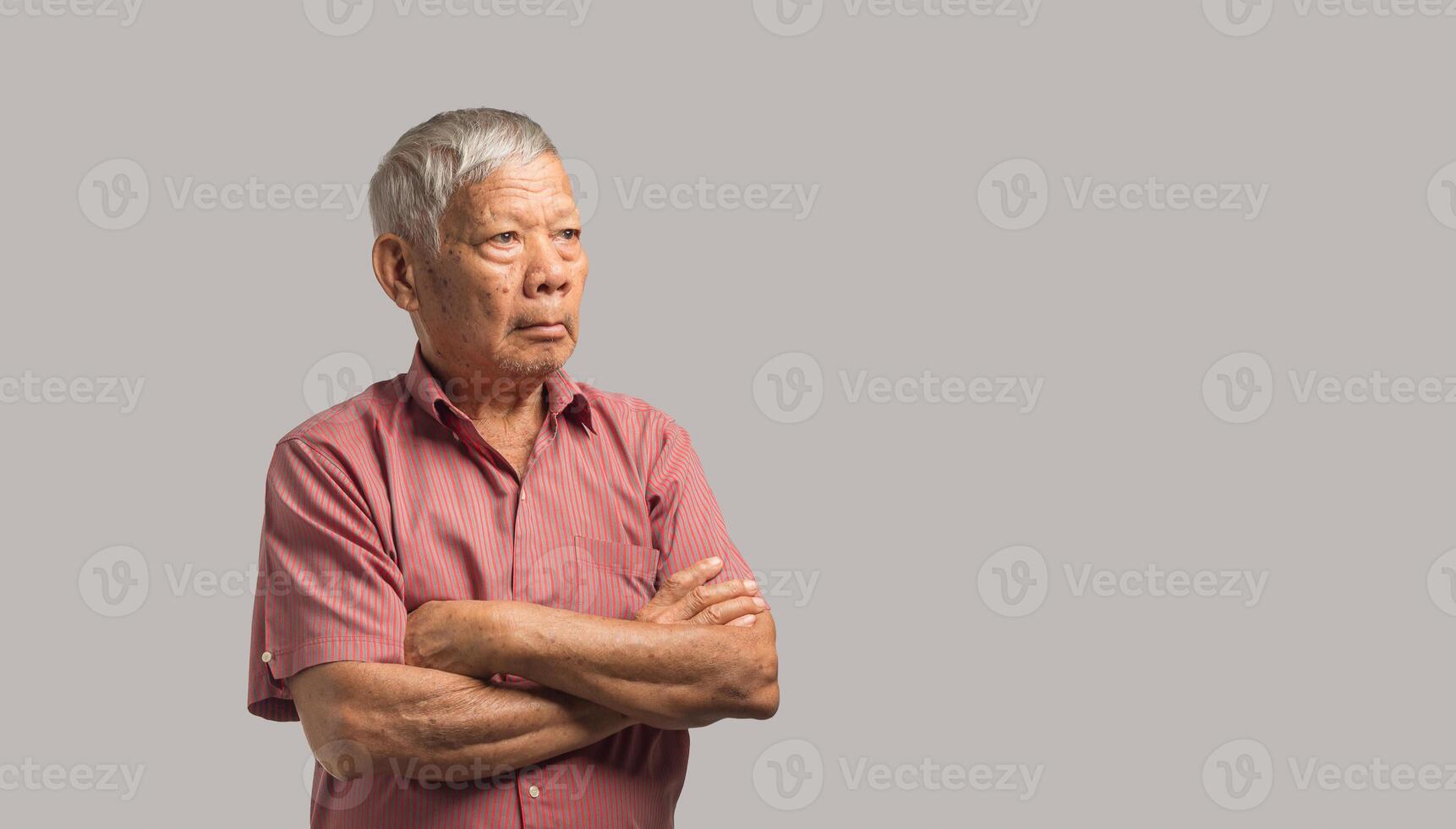 Senior man in a shirt is looking away while standing arms crossed on a gray background photo
