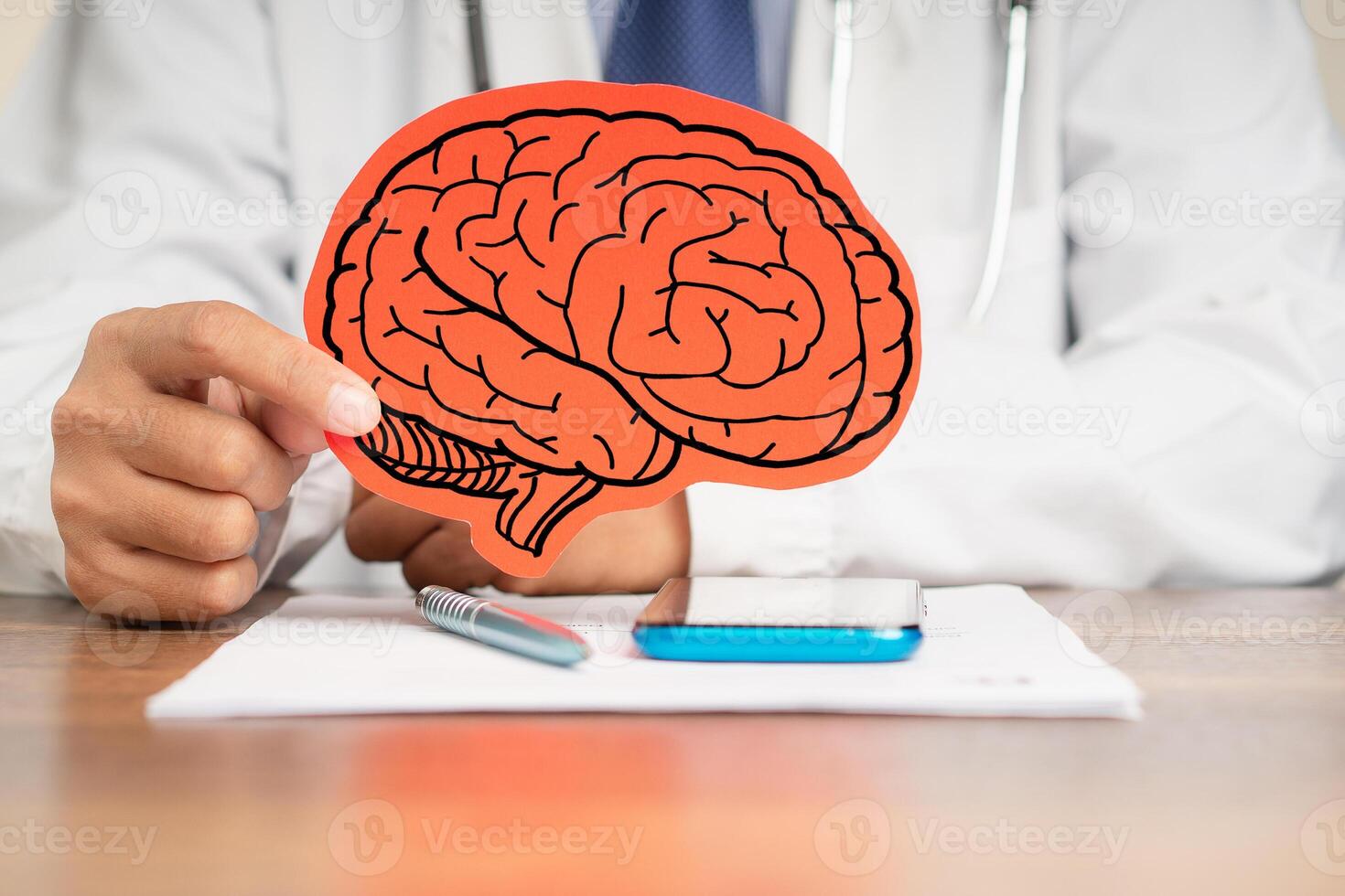 Doctor in a uniform holding a brain symbol made from red paper while sitting at the table. photo