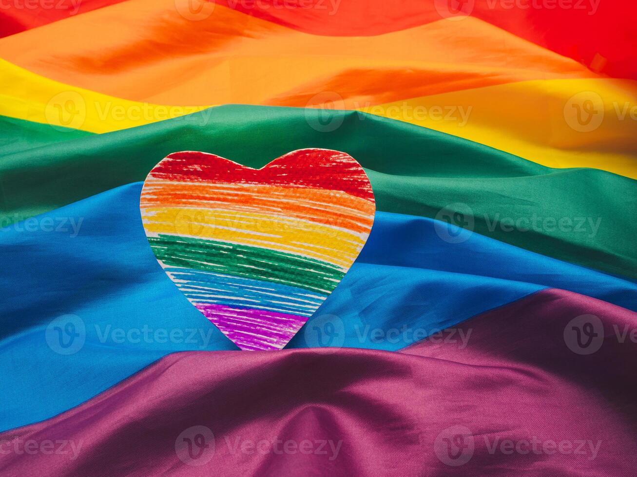 Close-up of a rainbow heart shape symbol made from paper over the rainbow flag or LGBT flag photo
