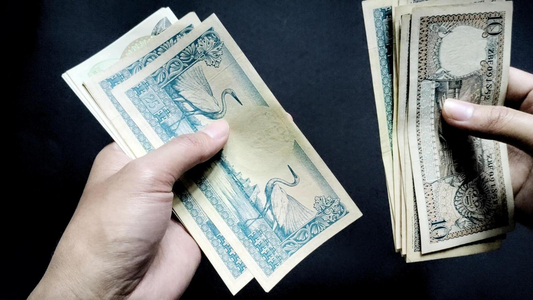 Top view of a person's hand is seen counting old rupiah banknotes of Rp 10 and Rp20, isolated on a black background. photo