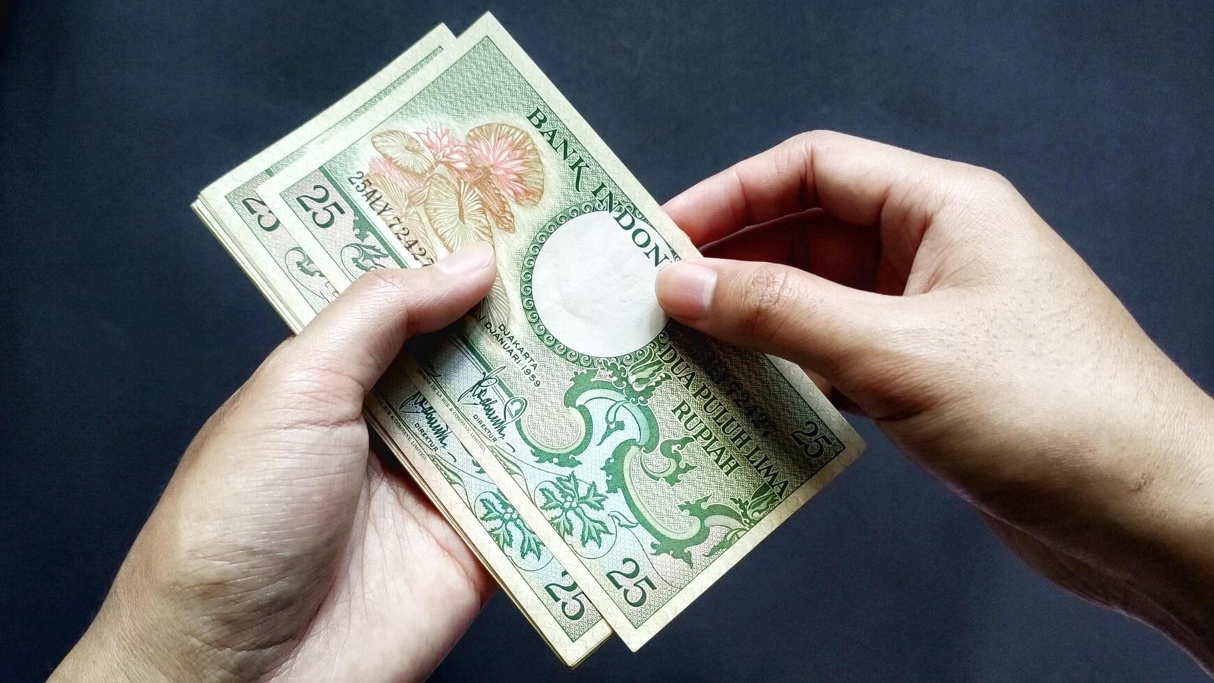 Portrait of a man holding old rupiah banknotes of Rp 25 rupiah denomination, isolated on a black background. Close up view photo