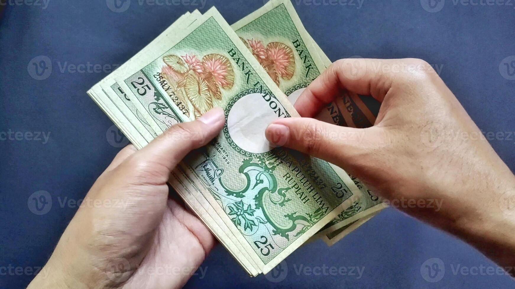 Top view of a man hand counting several old rupiah banknotes of Rp 25 rupiah denomination, isolated on a black background photo