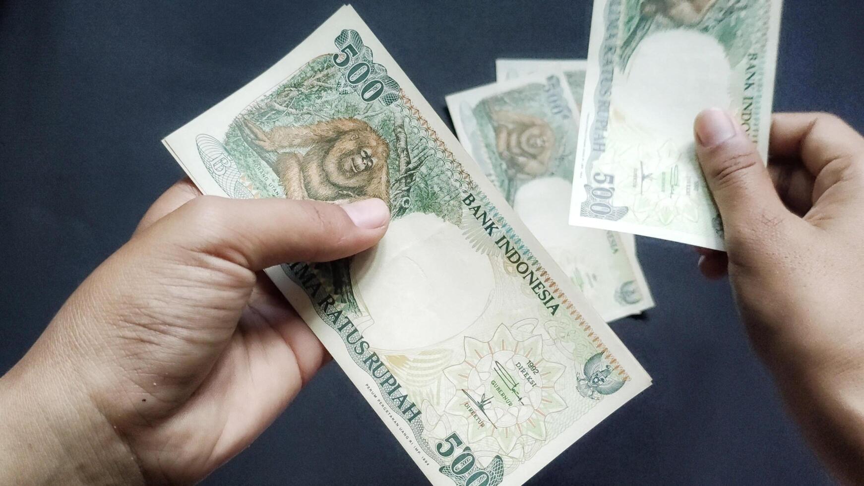 Portrait of a person's hand counting old rupiah banknotes of Rp500,00 isolated on a black background. photo