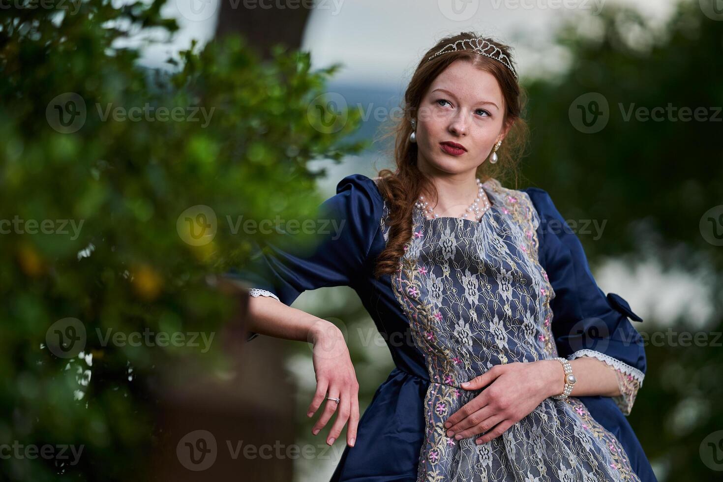 Portrait of a young long red hair girl in Victorian style dress posing beside castle photo