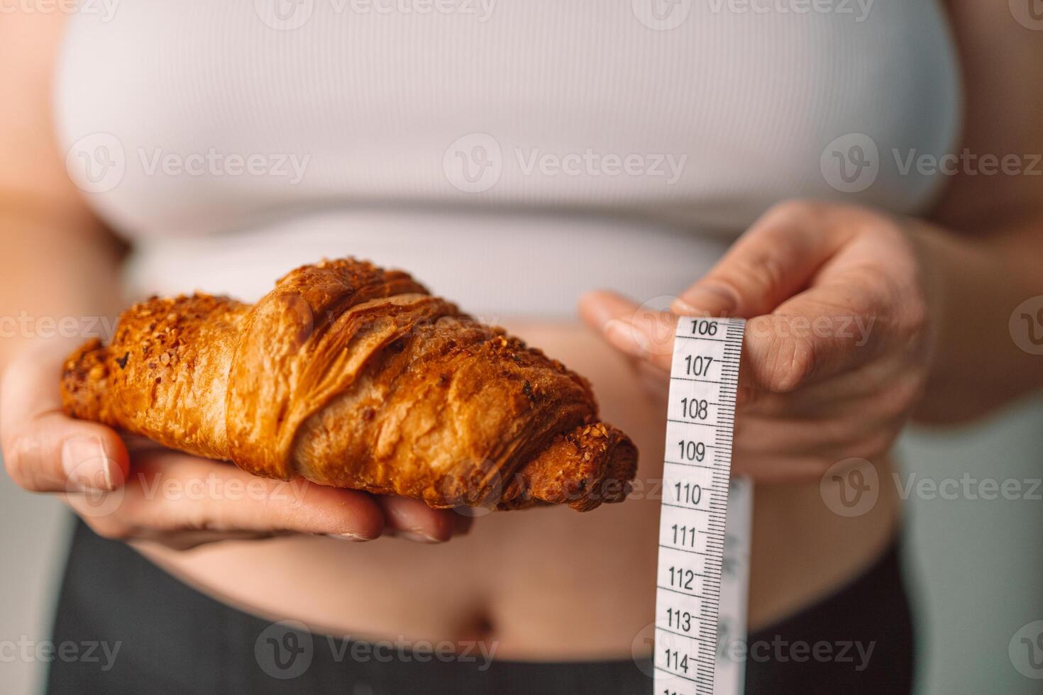 Woman holding croissant and measuring tape, unhealthy eating concept photo