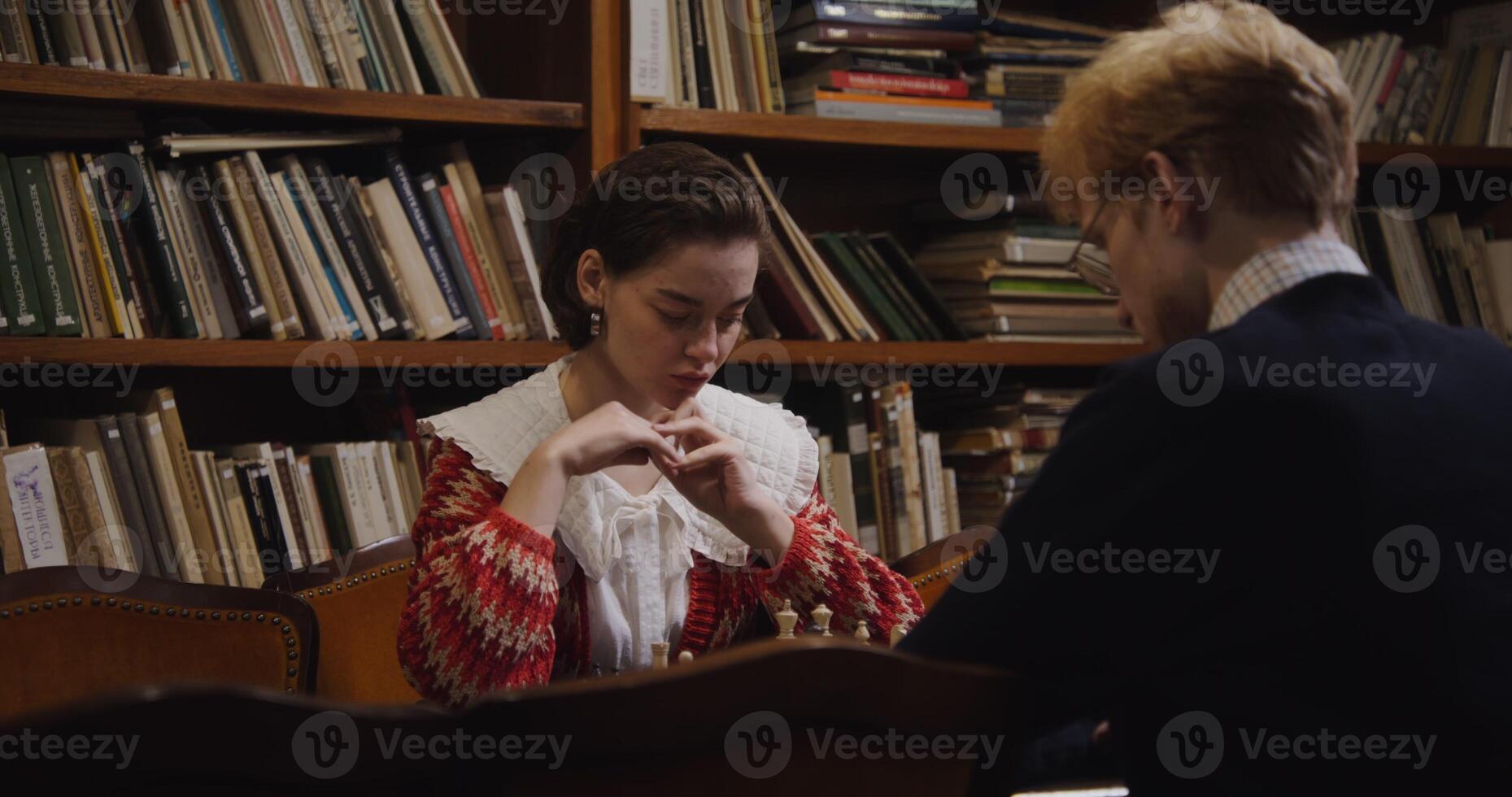 A woman playing chess with a man in front of bookshelves photo