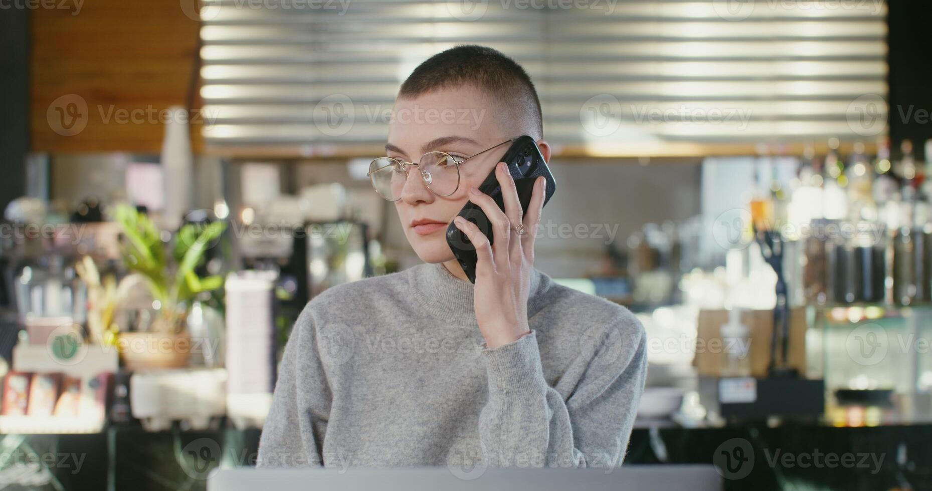 A woman in glasses talking on the phone while sitting at a table photo