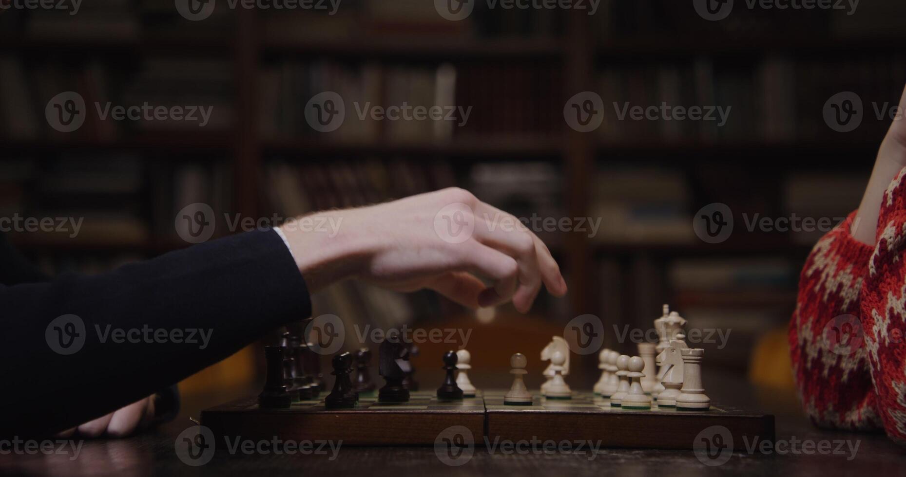 A man and woman playing chess in front of a bookcase photo