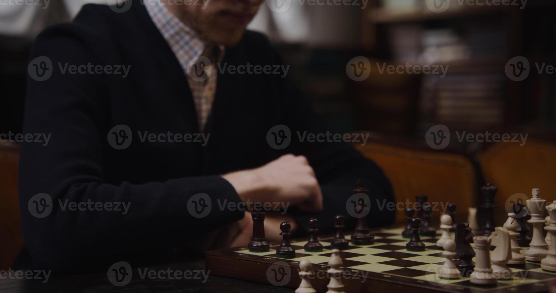 A man in a sweater sitting at a table with a chess board photo