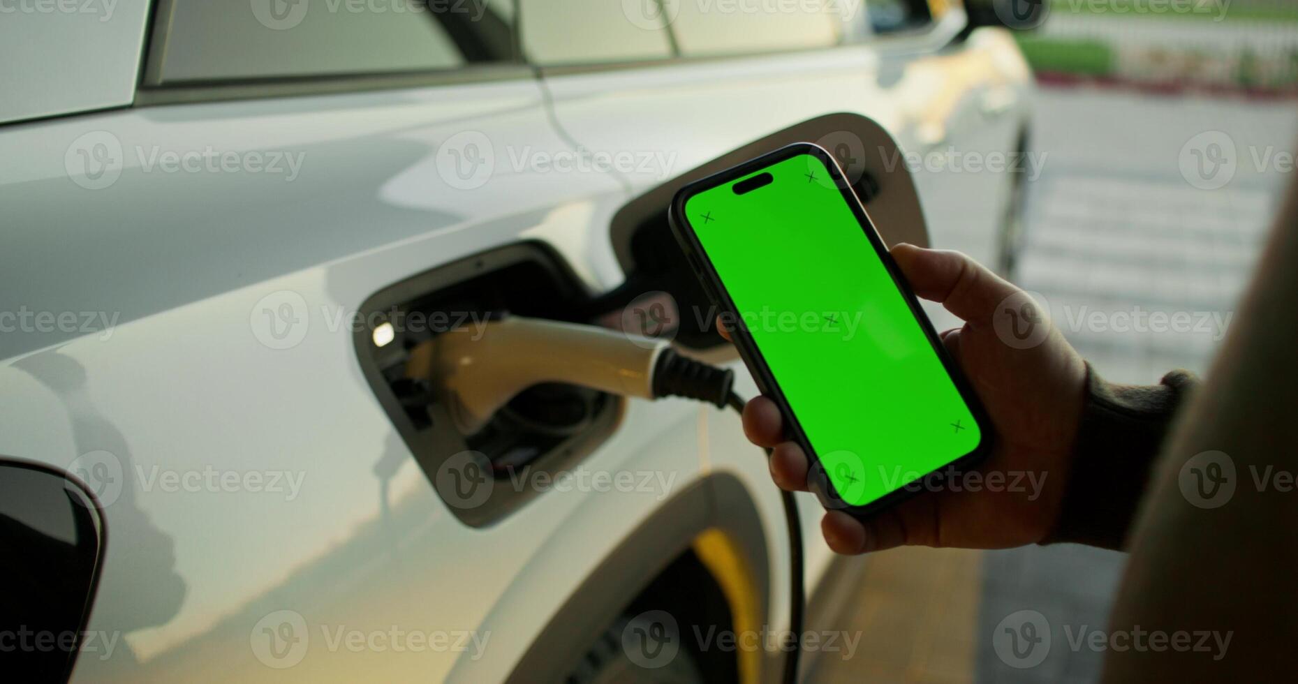 A man is charging his electric car with a smartphone in the background photo