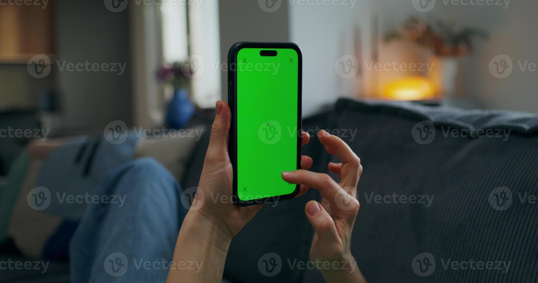 Woman using smartphone with green screen in living room photo
