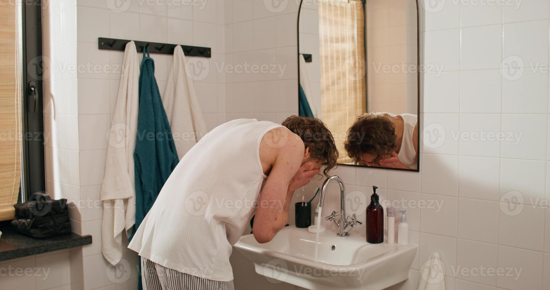 A man is washing his face in a bathroom sink photo