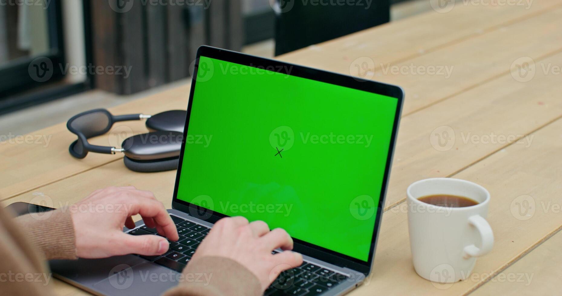 Man using laptop with green screen on wooden table photo