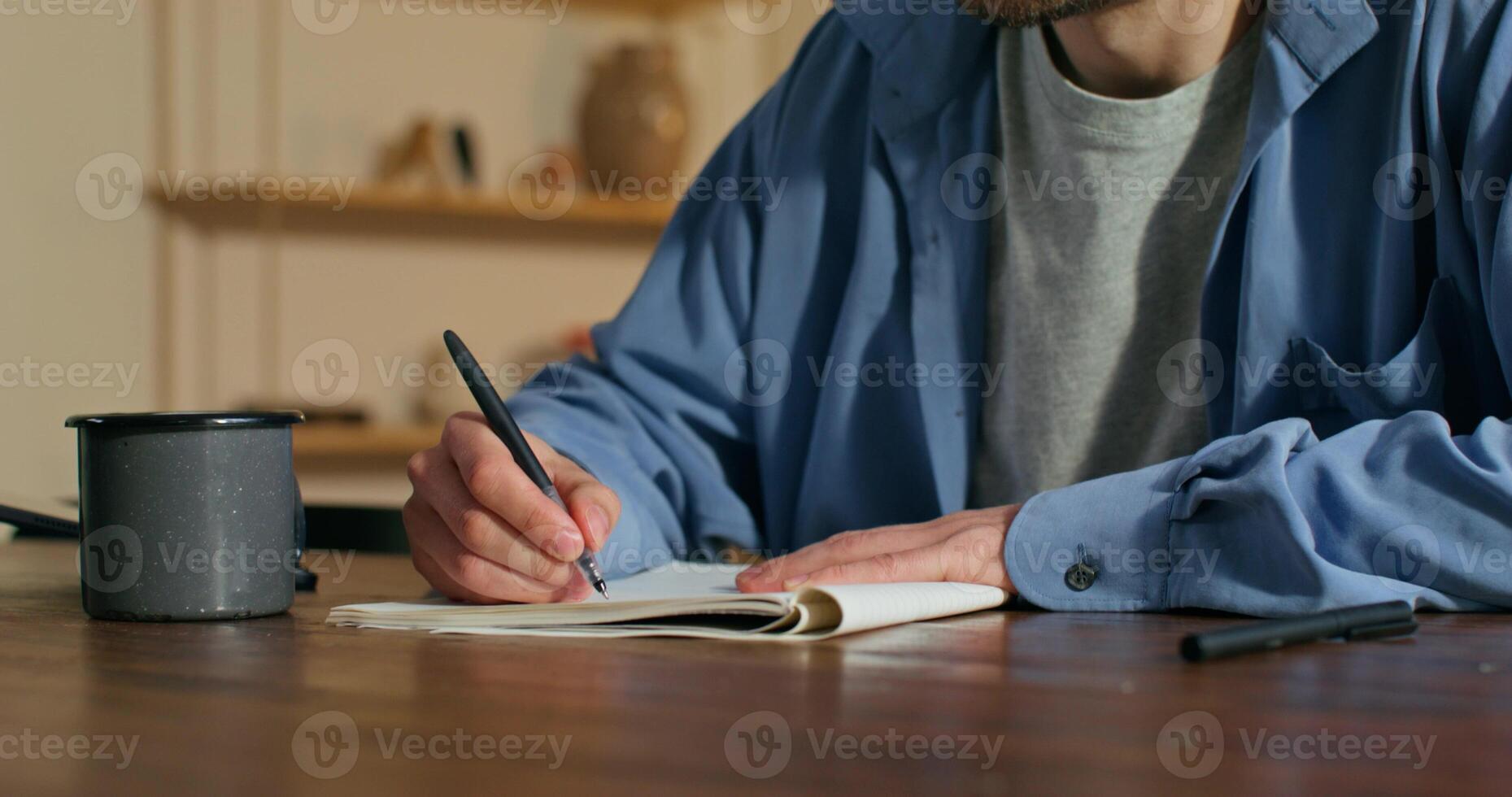 A man is writing in a notebook with a pen photo