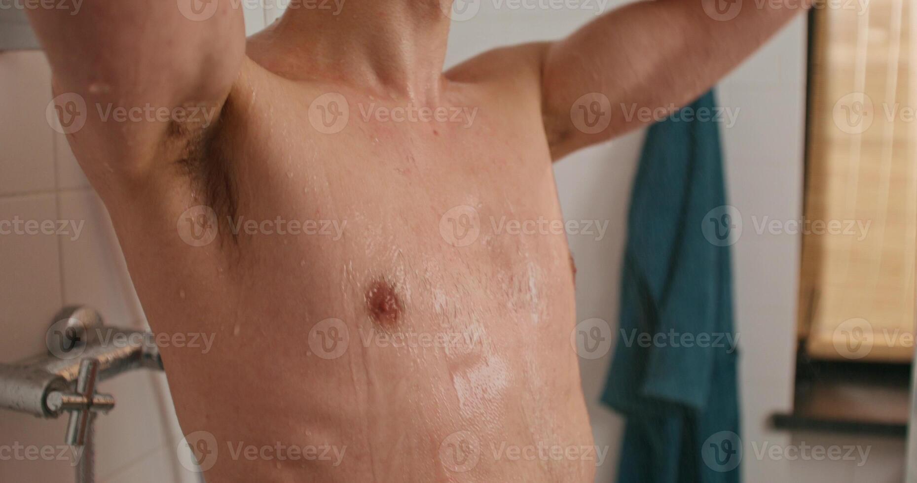 A man is standing in a shower with his shirt off photo