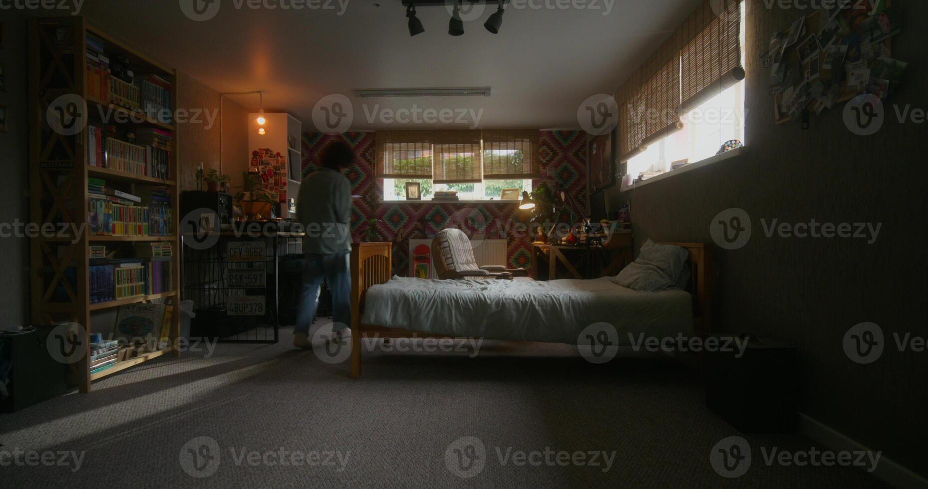 A person standing in a room with a bed and a desk photo