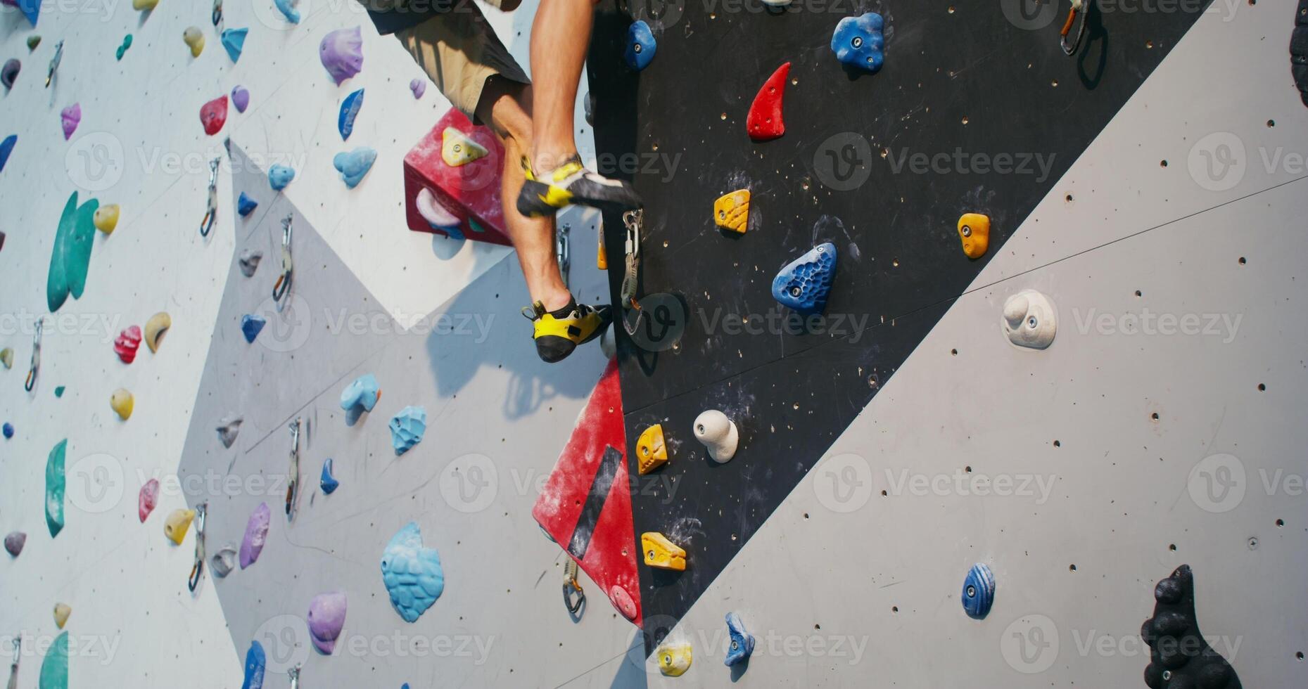 A young man wearing a safety belt, gently descends down the climbing wall photo