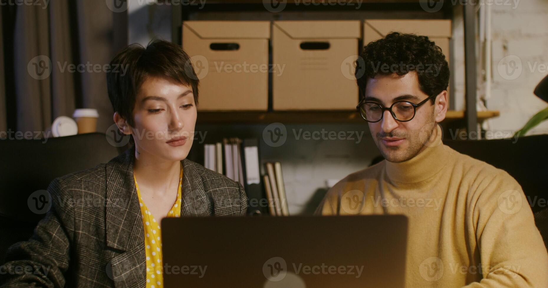 Two young colleagues work together sitting at a table in front of an open laptop photo