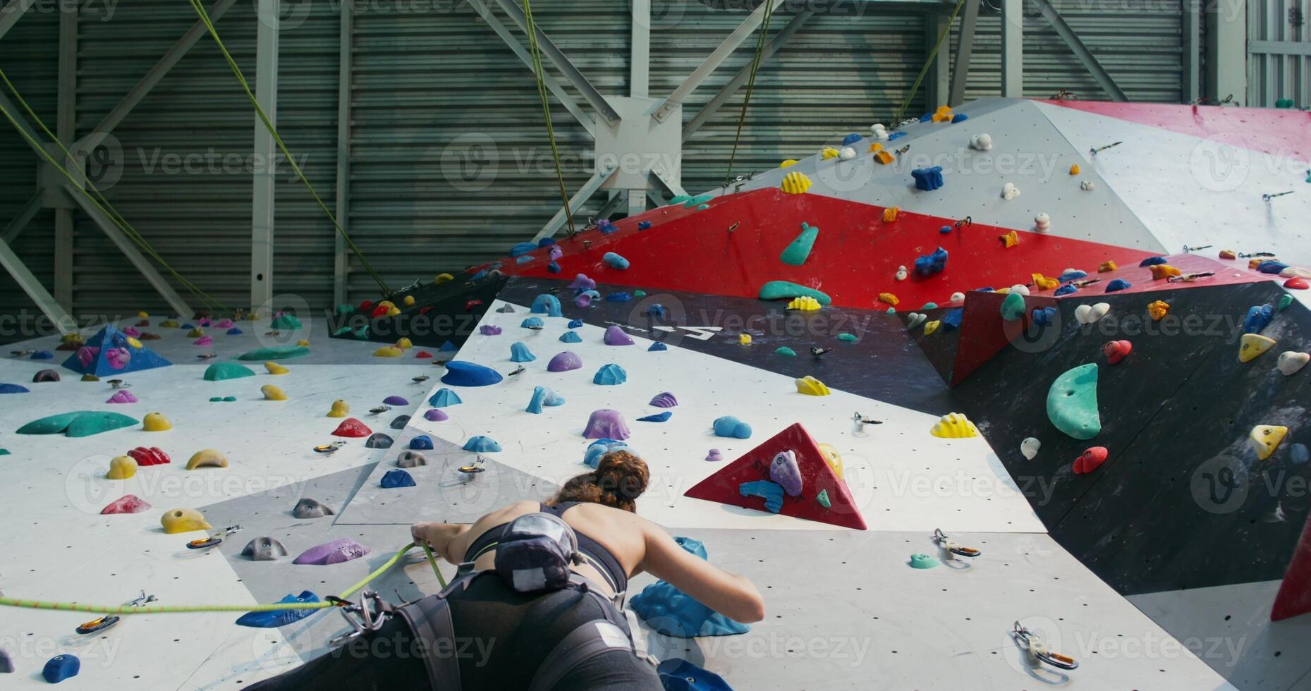 A young woman athlete climbing a climbing wall and attaching a rescue rope photo