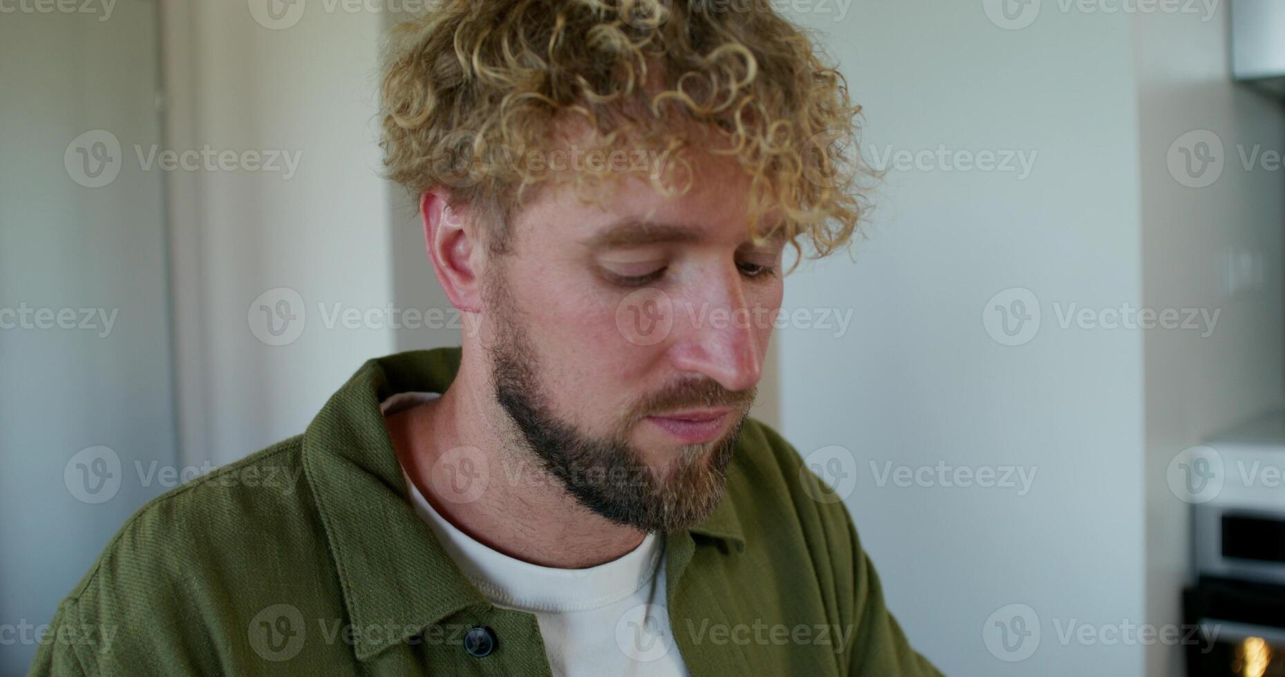 A man with curly hair and a beard is looking down photo