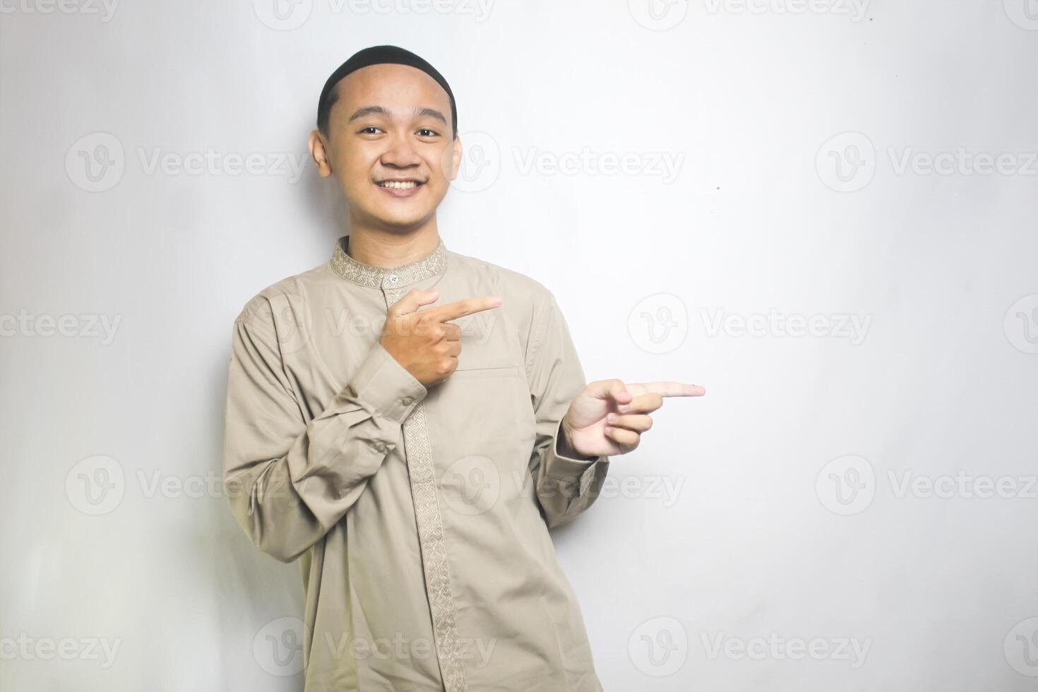 Muslim Man with Hand Gesture of Pointing Right Wearing a Beige Islamic Shirt and Black Cap photo