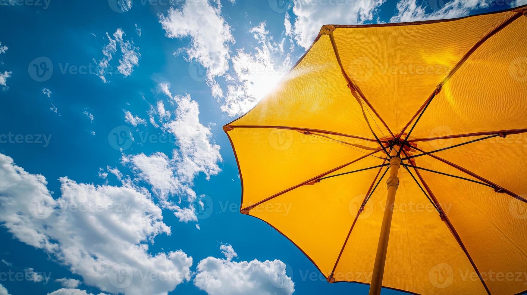 Bright sunlight shining through yellow umbrella against blue sky with fluffy clouds photo