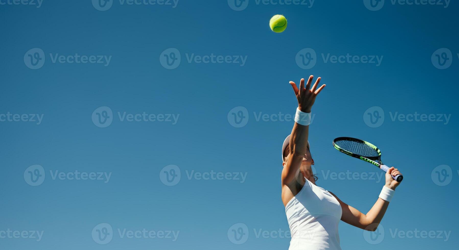Female tennis player serving ball under clear blue sky photo