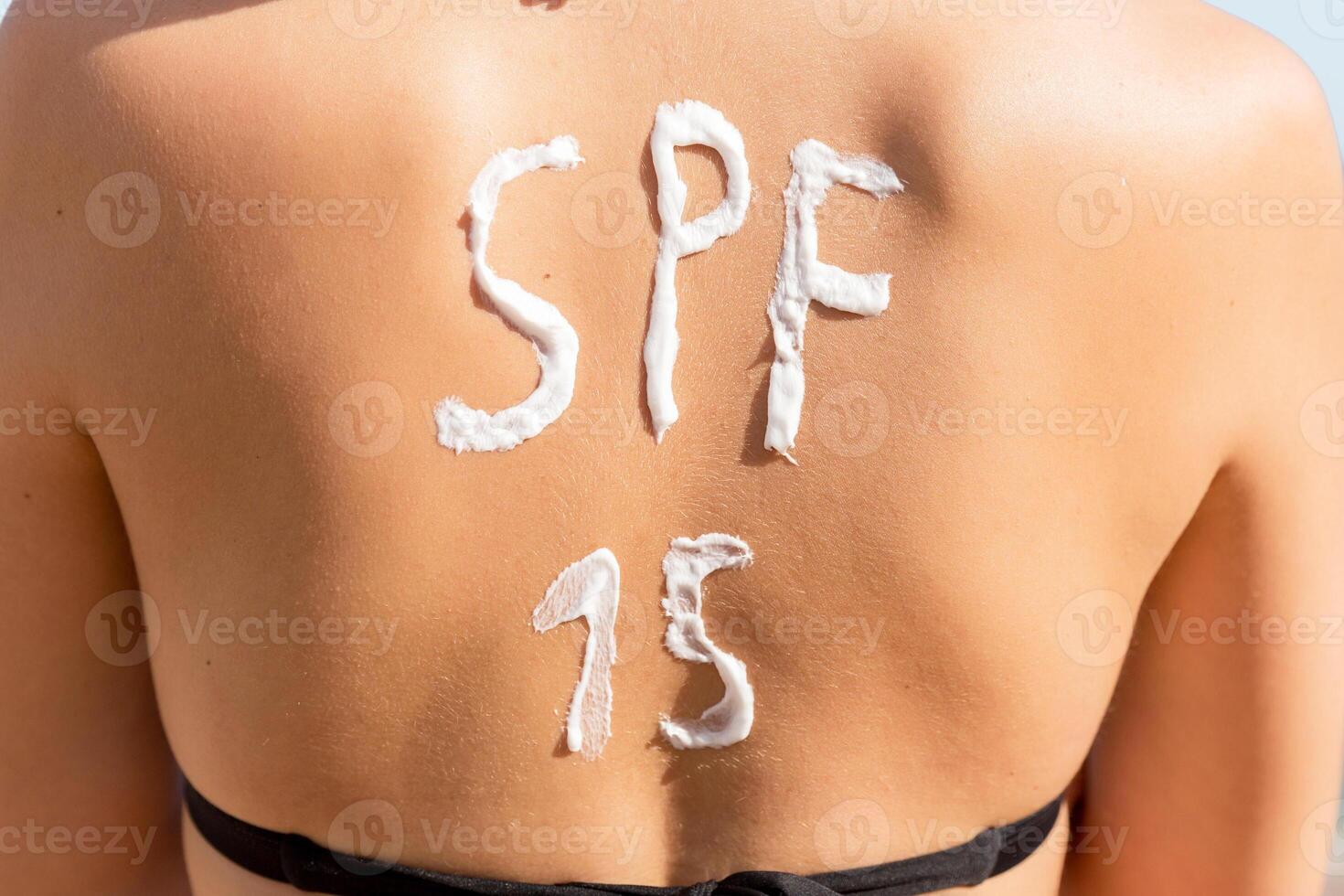 Pretty woman has spf 15 word made of sun cream on her back at the beach photo
