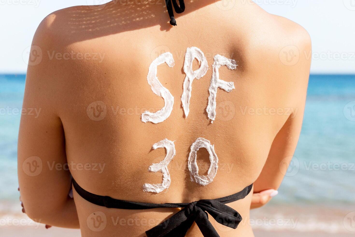 Spf 30 word is drawn with sunblock on woman's back relaxing at the beach photo