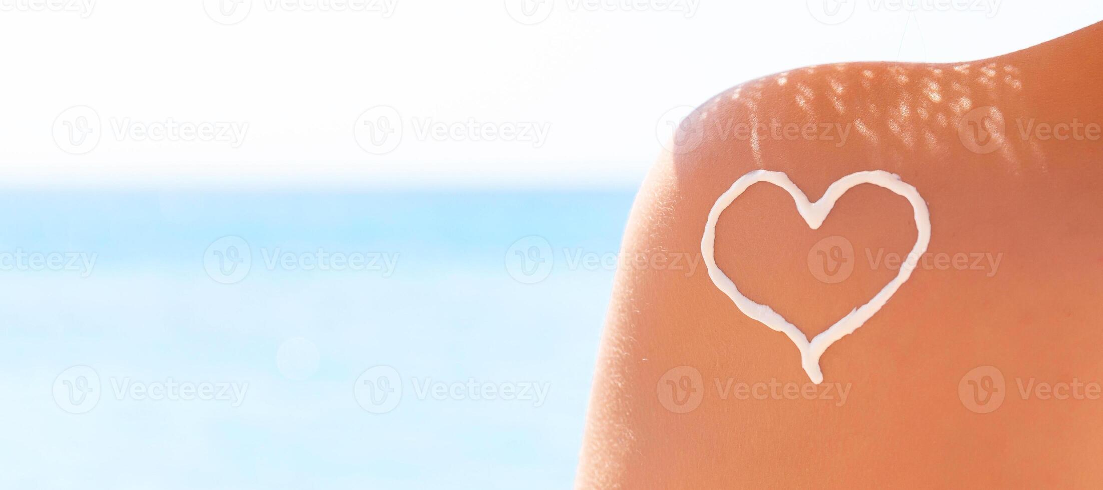 Heart made of sun cream is drawn on woman's shoulder at the beach photo