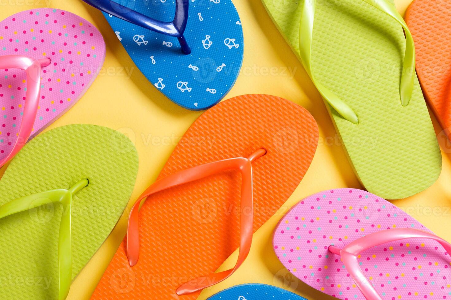 many colored flip flops on yellow background.Copy space top view photo