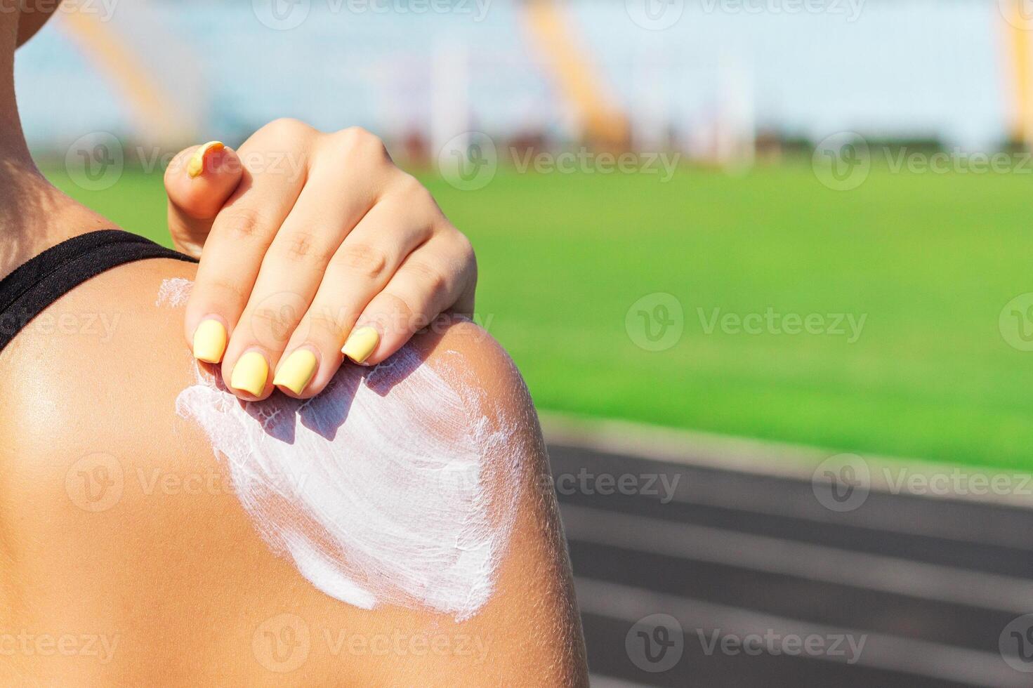 Fitness woman applying sunscreen on her shoulder before training at the stadium. Protect your skin during sport activity photo