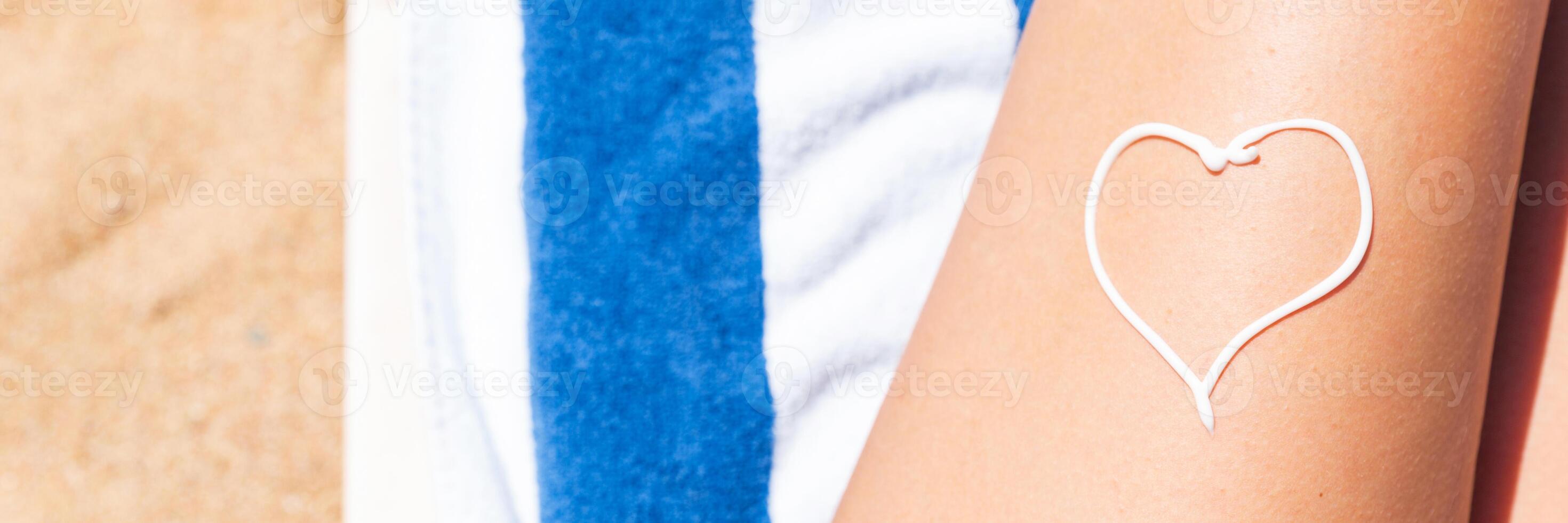 Sunscreen the form heart on woman's leg sunbathing the towel by the sea photo