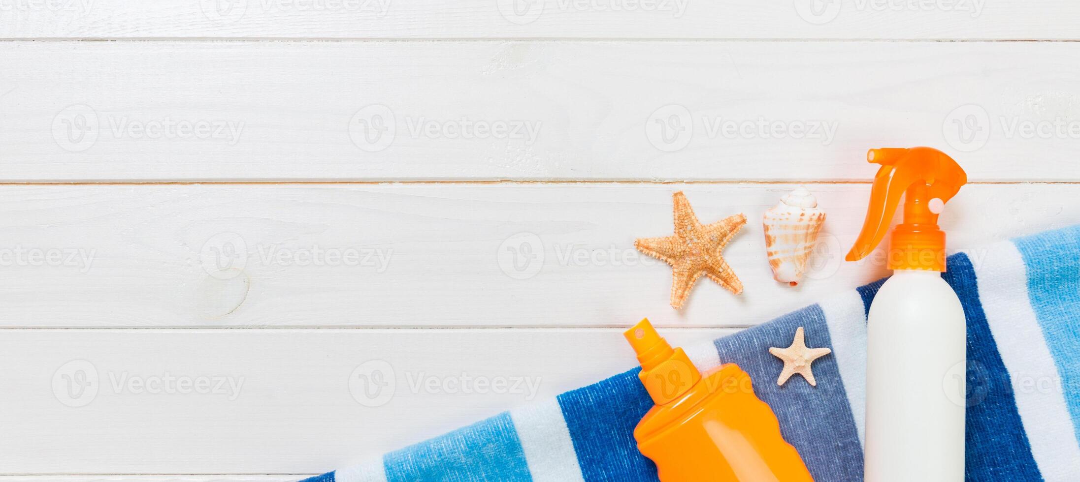 Sunscreen bottles with starfish and blue towel on white wooden table banner with copy space. Travel healthcare accessories top view photo