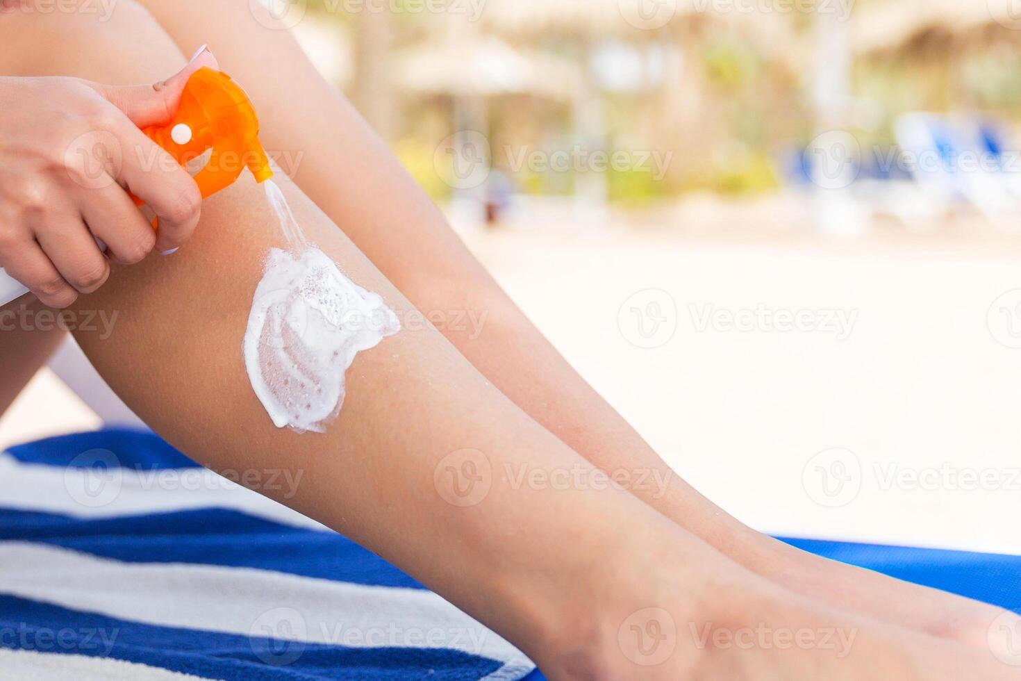 Girl is sitting on the sunbed and applying sun cream her leg at the beach photo