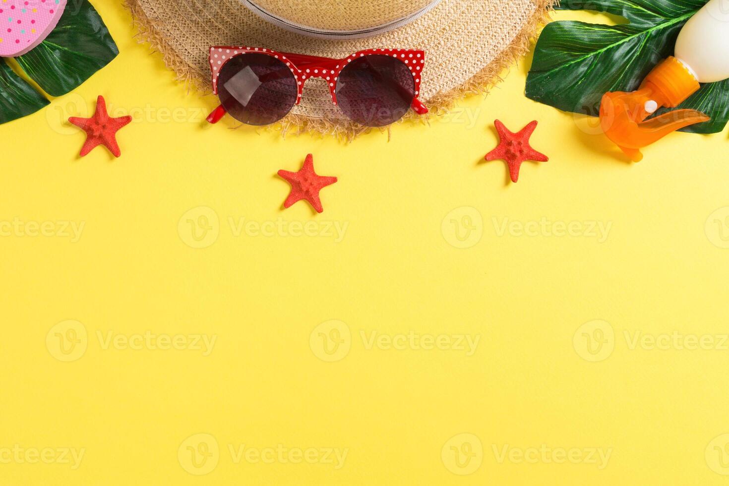 Beach accessories with straw hat, sunscreen bottle and seastar yellow background top view with copy space photo