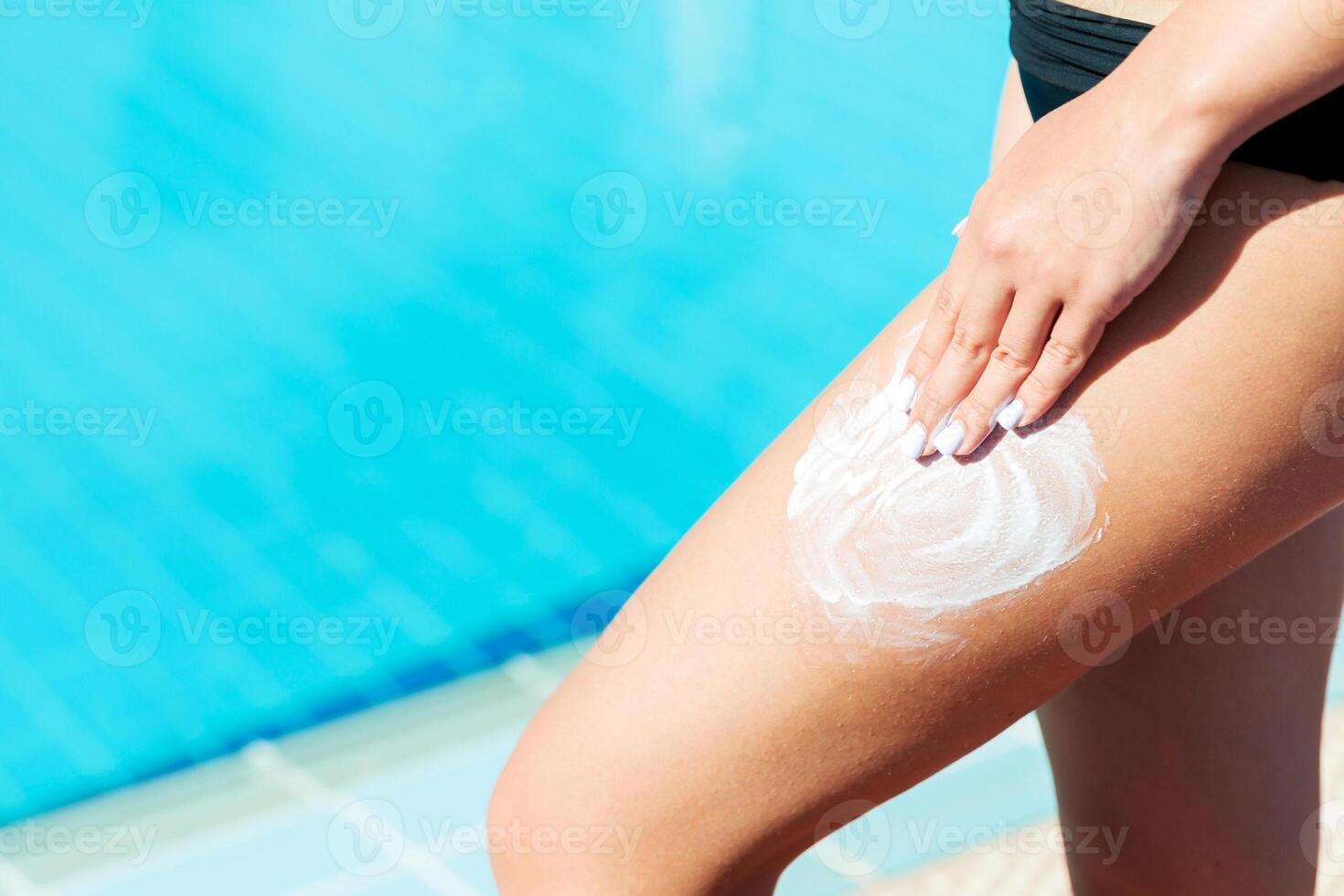 Female hand applying sunscreen cream leg by the swimming pool. Sun Protection Factor in vacation, concept photo