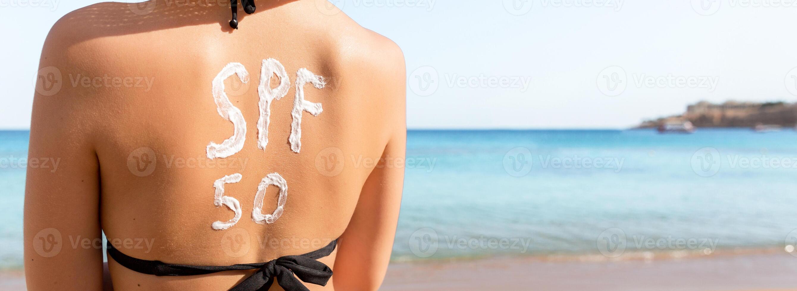 Woman with sunscreen in form of SPF 50 word on her back sunbathing at the beach. Sun protection factor concept photo