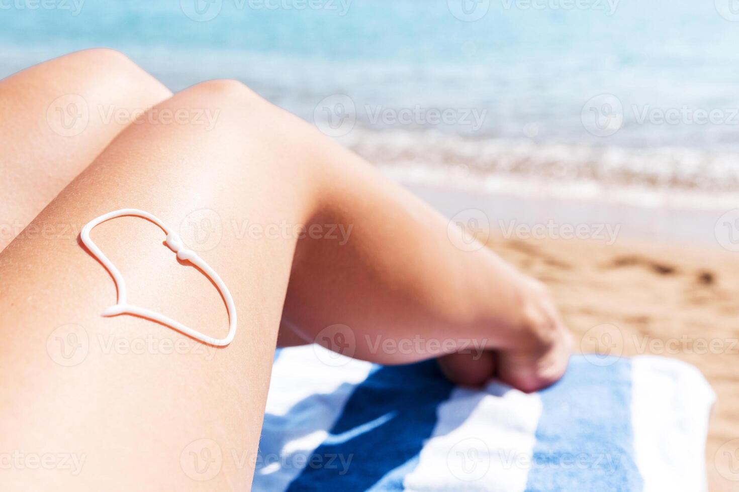 Sunscreen the form of heart on woman's leg sunbathing on the towel by the sea photo