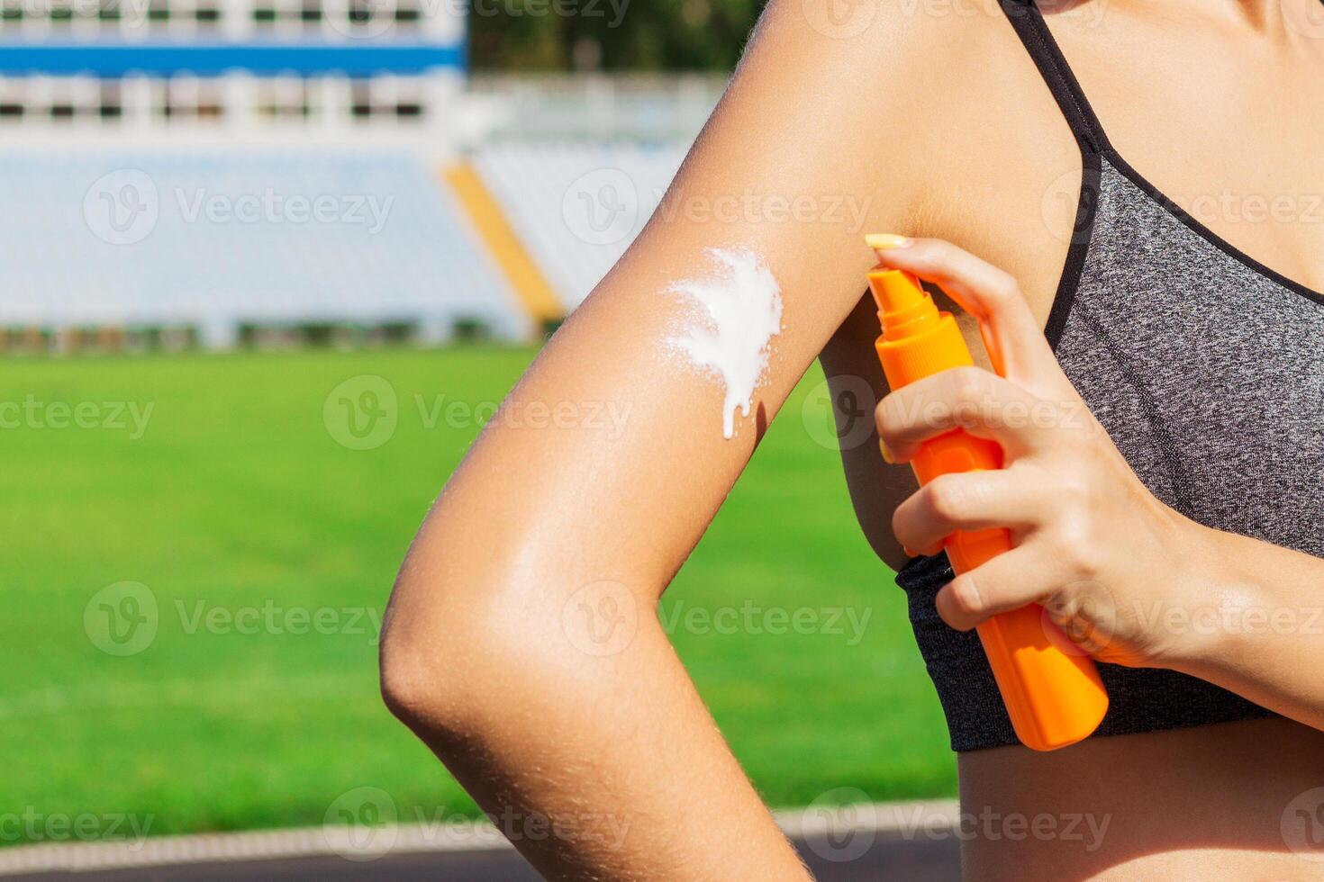 Young woman applying sunscreen her arms before physical activities at the stadium. Protect your skin from sunburn photo
